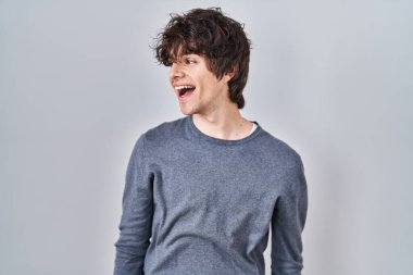 İzole edilmiş arka planda duran genç adam yüzünde gülümseme ve doğal ifadeyle yan yana bakıyor. Kendinden emin gülen. 