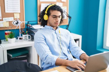 Ofiste çalışan dizüstü bilgisayar ve kulaklık kullanan genç Latin bir iş adamı.