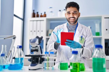 Laboratuvarda dokunmatik ped kullanan genç bir İspanyol bilim adamı üniforması giyiyor.