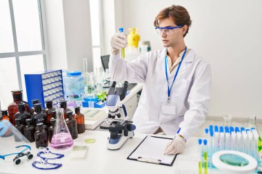 Young caucasian man scientist holding test tube writing on document at laboratory