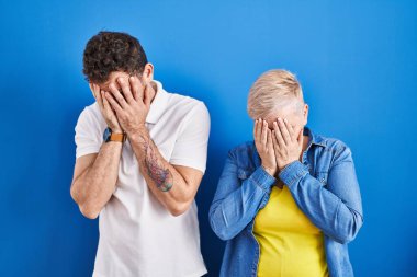 Genç Brezilyalı anne ve oğlu mavi arka planda dikiliyor. Ağlarken yüzünü ellerle kapatıyor. depresyon kavramı. 