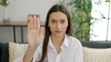 Kanepede oturan genç ve güzel İspanyol kadın ciddi bir ifadeyle ve evde jesti durdurun.