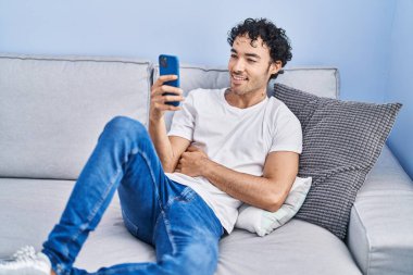Evdeki kanepede oturan, akıllı telefon kullanan genç bir İspanyol.