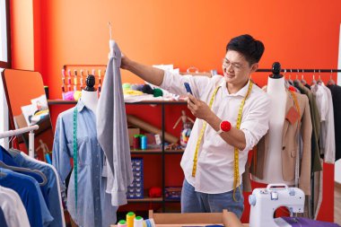 Genç Çinli terzi atölyeden gömleğe akıllı telefondan fotoğraf çeker.