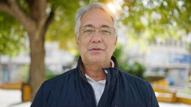 Gri saçlı orta yaşlı bir adam parkta kameraya konuşuyor.