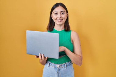 İspanyol kız bilgisayarla çalışıyor. Pozitif ve mutlu görünüyor. Dişlerini gösteren bir gülümsemeyle ayakta duruyor. 