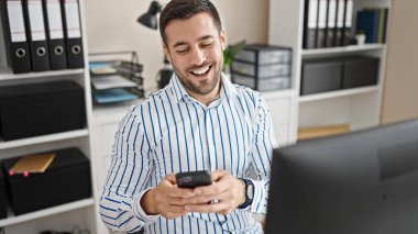 Genç İspanyol iş adamı ofiste gülümseyen akıllı telefon kullanıyor.