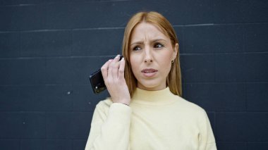 Akıllı telefondan gelen sesli mesajı dinleyen genç sarışın kadın izole edilmiş siyah arka planda ciddi bir ifadeye sahip.