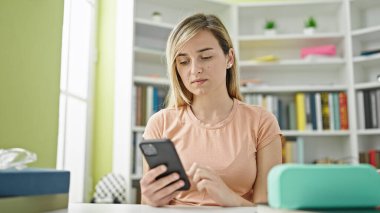 Young blonde woman student using smartphone at library university