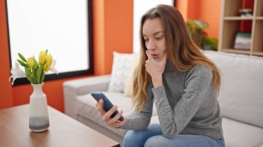 Young caucasian woman using smartphone with serious expression at home