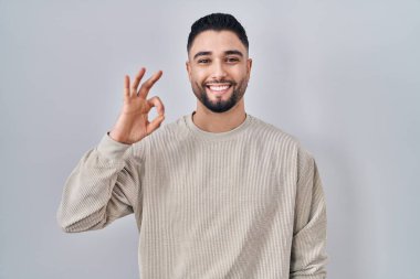 İzole edilmiş arka planda duran yakışıklı genç adam gülümsüyor ve el ve parmaklarıyla 