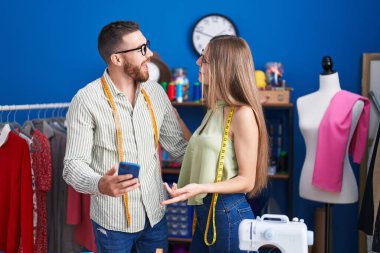 Man and woman tailors smiling confident using smartphone at clothing factory