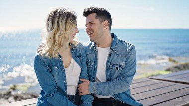 Erkek ve kadın çift birbirlerine sarılıyorlar. Sahilde bankta oturuyorlar.