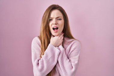 Young caucasian woman standing over pink background shouting suffocate because painful strangle. health problem. asphyxiate and suicide concept.  clipart