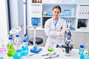 Young brunette woman working at scientist laboratory skeptic and nervous, disapproving expression on face with crossed arms. negative person. 