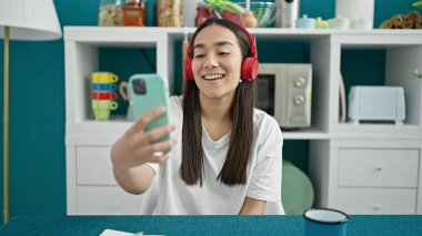 Genç, güzel, İspanyol bir kadın yemek masasında oturmuş müzik dinliyor.