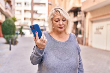 Sokakta akıllı telefon kullanan orta yaşlı sarışın kadın.