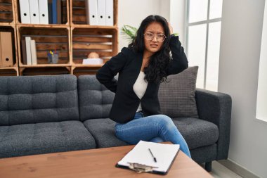 Konsültasyondaki genç Asyalı kadın boyun ağrısı çekiyor. Boynuna elle dokunuyor. Kas ağrısı var. 