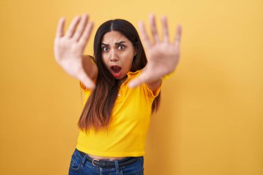 Sarı arka planda duran genç Arap kadın avuç içi hareketlerini durduruyor, kızgın ve hayal kırıklığına uğramış yüz ifadesi. 