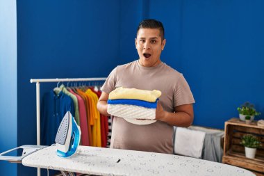 Şok olmuş suratıyla ütüledikten sonra çamaşır katlayan İspanyol genç adam şüpheci ve alaycı görünüyor, ağzı açık kalınca şaşırıyor. 