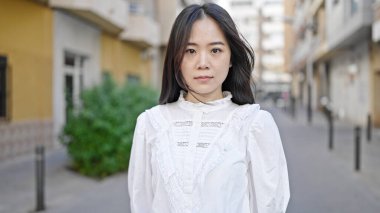 Young chinese woman standing with serious expression at street