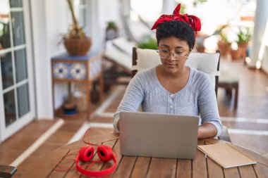 Afro-Amerikalı bir kadın evdeki terasta oturmuş ders çalışıyor.