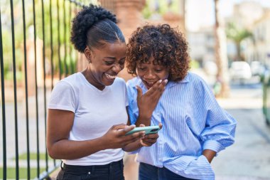Afrika kökenli Amerikalı kadın anne ve kız sokakta akıllı telefondan video izliyorlar.