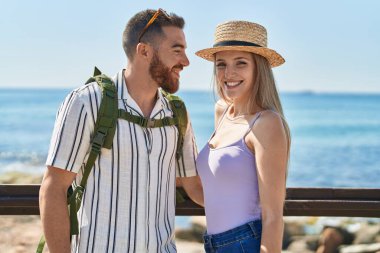Kadın ve erkek turist gülümsüyor. Deniz kenarında birbirlerine sarılıyorlar.