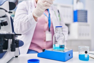 Young beautiful plus size woman scientist pouring liquid on test tube weighing liquid at laboratory