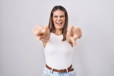 Beyaz arka planda duran İspanyol genç kadın seni ve kamerayı işaret ediyor, pozitif ve neşeli gülümsüyor. 