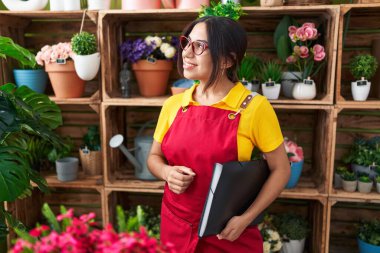 Young beautiful arab woman florist smiling confident holding binder at flower shop