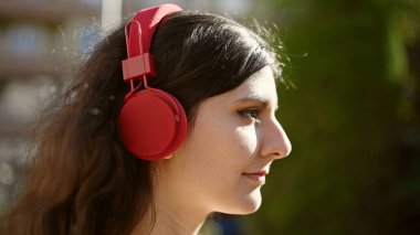 Young beautiful hispanic woman listening to music with serious expression at park