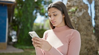 Genç, güzel, İspanyol bir kadın parkta akıllı telefon kullanıyor.