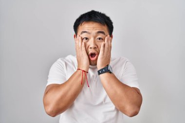 Beyaz arka plan üzerinde duran genç Çinli adam korkmuş ve şok olmuş, şaşırmış ve şaşırmış bir yüz ifadesi var. 