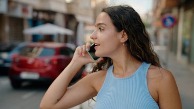 Genç, güzel, İspanyol bir kadın gülümsüyor ve caddede akıllı telefondan konuşuyor.