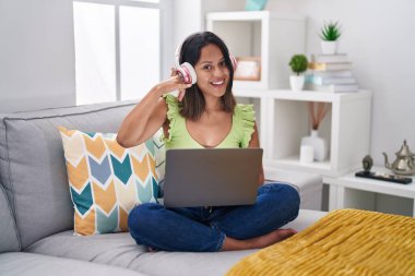 İspanyol genç kadın evde dizüstü bilgisayar kullanıyor gülümsüyor telefonla el ve parmak hareketleri yapıyor telefonda konuşuyor gibi. iletişim kavramları. 