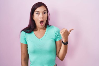 Pembe arka planda duran genç İspanyol kadın elleri yana doğru işaret ederek şaşırdı, ağzı açık hayret içinde kaldı.. 