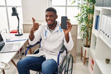 Tekerlekli sandalyede oturan Afrikalı Amerikalı doktor elinde akıllı telefonuyla mutlu ve olumlu gülümsüyor. 