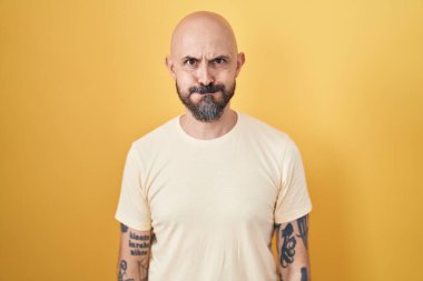 Sarı arka planda dikilen, komik yüzlü İspanyol dövmeli adam. Havayla şişmiş ağız, çılgın bir ifade.. 