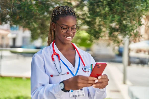 Parkta akıllı telefon kullanarak gülümseyen Afrikalı Amerikalı kadın doktor.