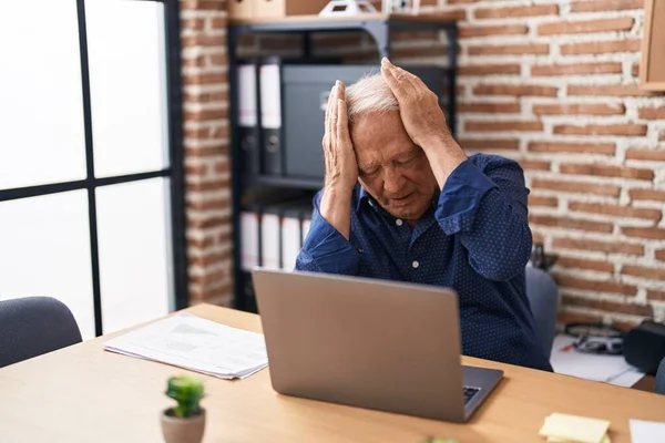 オフィスでコンピュータのラップトップを使用して作業灰色の髪を持つシニア男性は 痛みや片頭痛のために絶望的でストレスを受けています 手を頭に — ストック写真