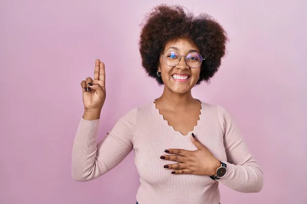 ピンクの背景に立つ若いアフリカ系アメリカ人の女性が胸と指で手で誓う忠誠の誓いを立てる — ストック写真