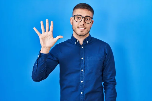 Jonge Spaanse Man Draagt Bril Blauwe Achtergrond Tonen Wijzen Met — Stockfoto
