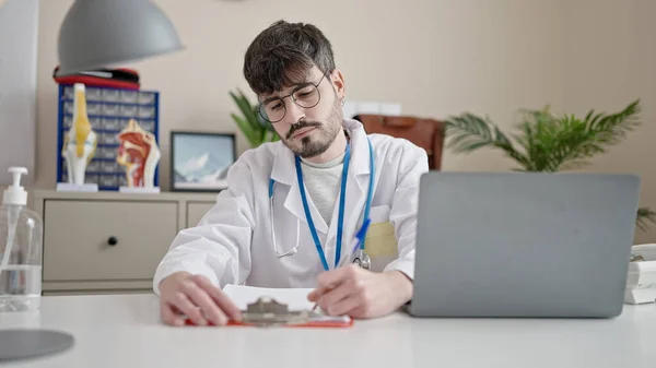 Νεαρός Ισπανόφωνος Γιατρός Χρησιμοποιώντας Laptop Γράφοντας Στο Πρόχειρο Στην Κλινική — Φωτογραφία Αρχείου