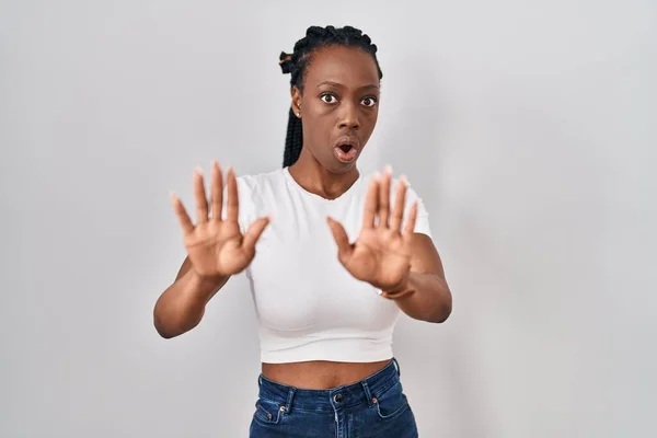 Beautiful black woman standing over isolated background moving away hands palms showing refusal and denial with afraid and disgusting expression. stop and forbidden.
