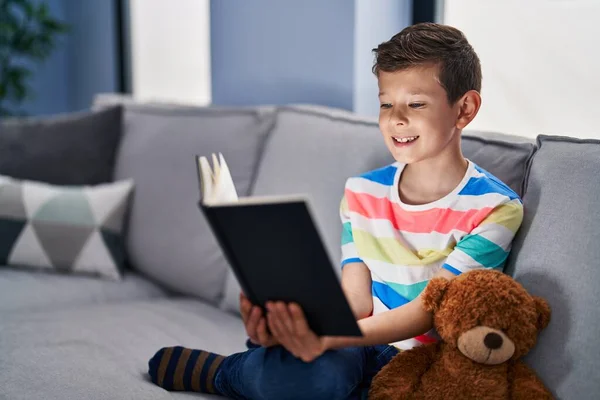ソファに座っている若い白人の子供は 幸せとクールな笑顔で笑顔の本を読んでいます 歯を見せて — ストック写真