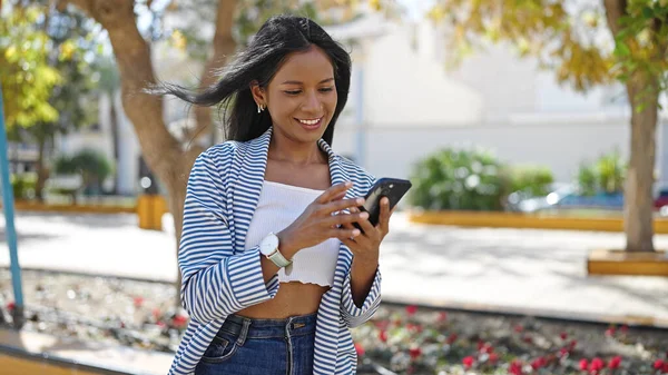 Afro-Amerikalı kadın parkta akıllı telefon kullanarak gülümsüyor.