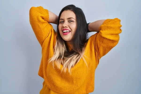 Young hispanic woman standing over isolated background relaxing and stretching, arms and hands behind head and neck smiling happy 