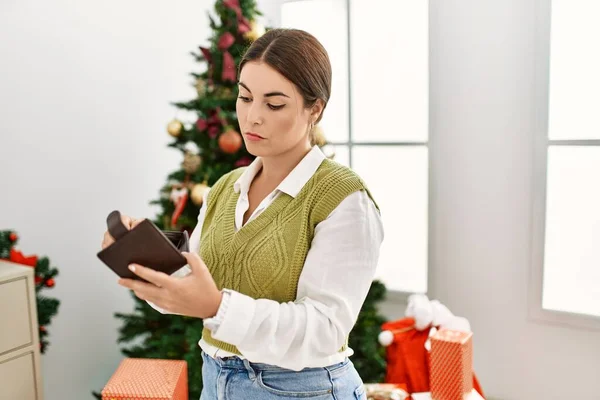 年轻美丽的惊慌失措的女人手里拿着钱包 站在圣诞树旁 — 图库照片