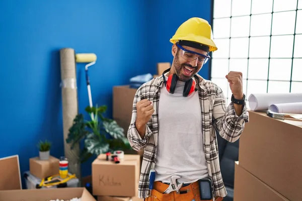 自宅の改装で働くひげを持つ若いヒスパニック系の男性は非常に満足し 腕を上げて勝者のジェスチャーを行う興奮し 笑顔と成功のために叫んでいます お祝いのコンセプト — ストック写真